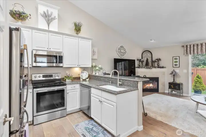 Open-concept kitchen featuring quartz counters, stainless steel appliances, breakfast bar seating, & soaring ceilings.