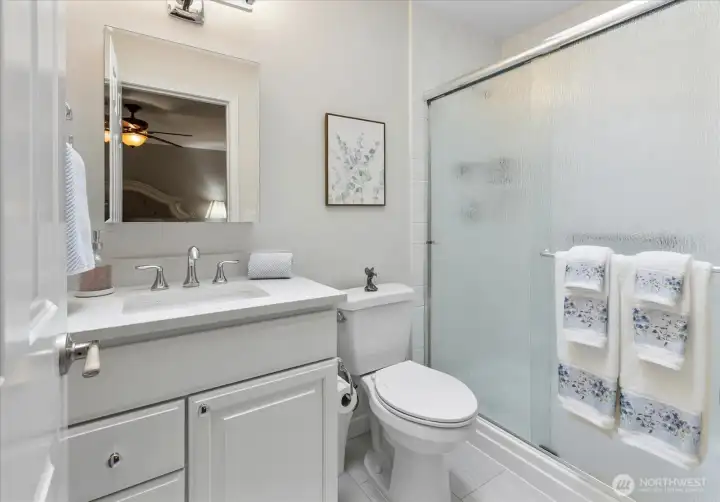 Updated ensuite bathroom with modern vanity, sleek fixtures, tile flooring, & glass-enclosed shower.