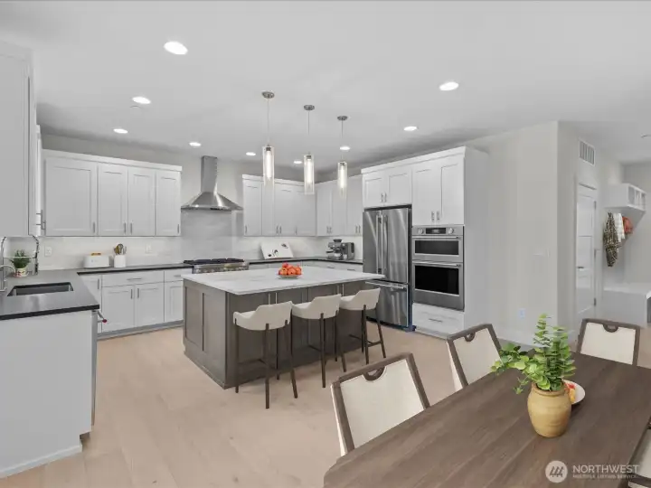 Stunning open-concept kitchen showcasing custom LCM cabinets painted in crisp white and high-end KitchenAid stainless steel appliances. The design shines with an Arctic White quartz center island paired with unique, textured leather-finish quartz perimeter countertops, perfectly connecting the kitchen to the casual dining space. Virtually staged.