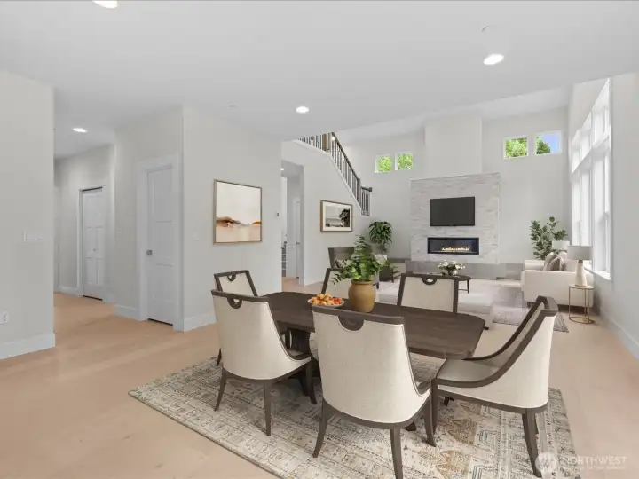 A beautiful perspective looking from the casual eating area into the light-filled Great Room. The view highlights the home's open-concept design, soaring two-story ceilings, and dramatic floor-to-ceiling stone fireplace surround. Virtually staged.