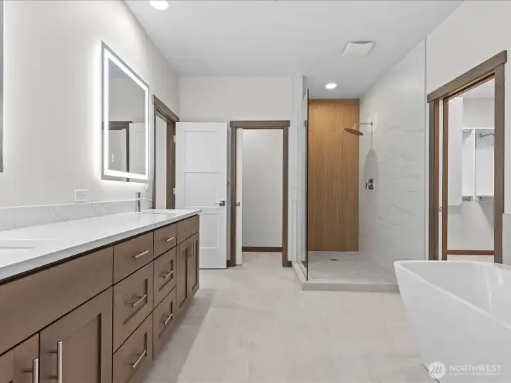 Another stunning view of the primary suite bath, highlighting the excellent storage, crisp quartz counters, contemporary tiling, elegant glass-enclosed shower and a relaxing soaking tub.