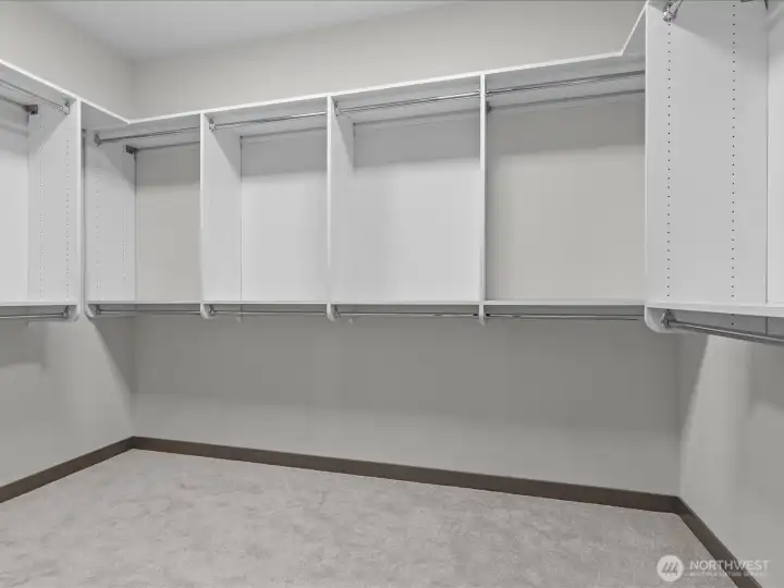 Generously sized primary walk-in closet featuring extensive custom built-in shelving, ample hanging rods, and a clean, organized design that maximizes storage.