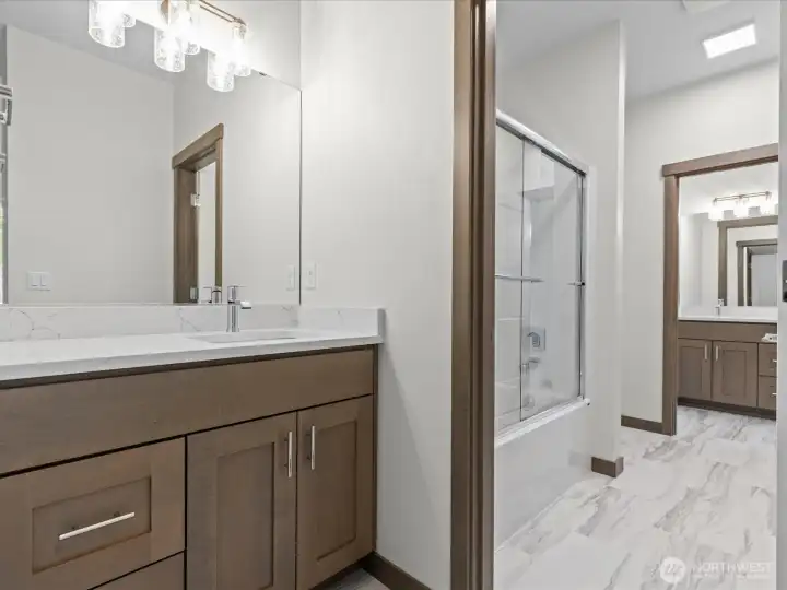 A smart and functional upstairs Jack and Jill bathroom layout. This design features a private, individual sink and vanity station that leads directly into the shared tub/shower and toilet area, seamlessly connecting the upper-level rooms.
