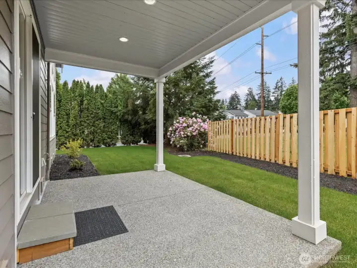 Step outside to a spacious, covered concrete patio perfect for year-round outdoor dining and entertaining. Overlooks a beautifully maintained, fully fenced backyard with a lush green lawn and privacy landscaping.