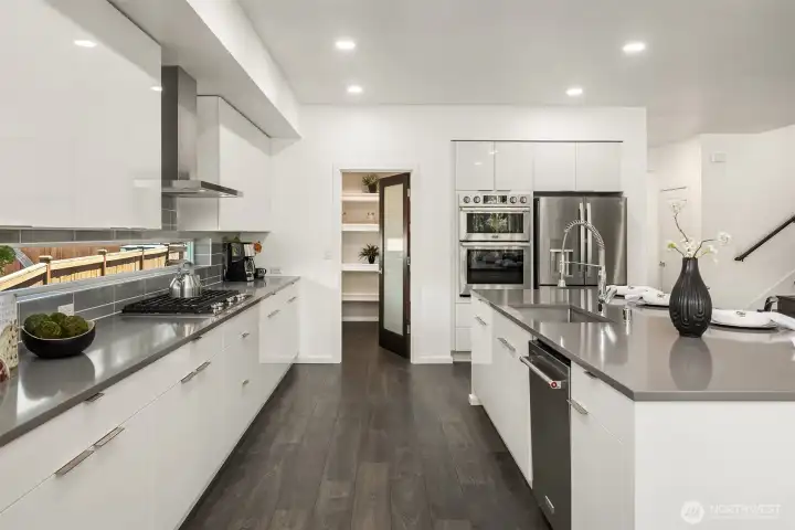 Designer kitchen features glossy cabinetry, quartz-style counters, stainless appliances, expansive island seating, and clean modern lines.
