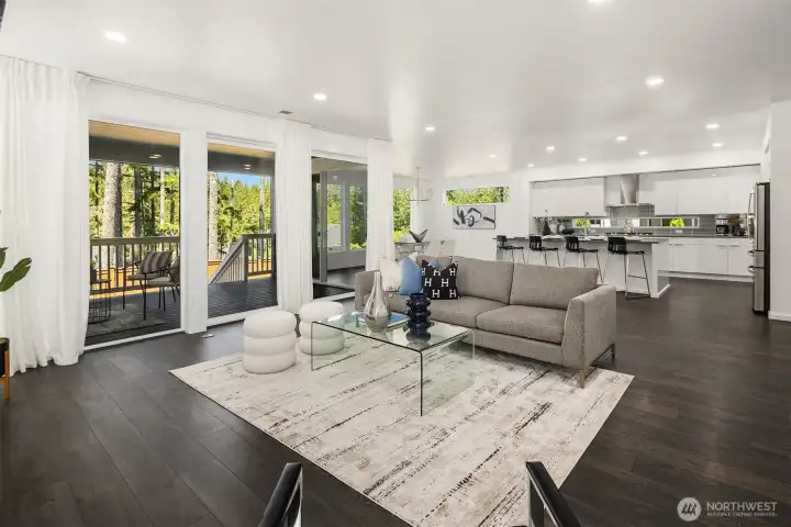Open great room features a sleek fireplace, wide-plank flooring, abundant natural light, and seamless flow to the kitchen, dining area, and Signature Outdoor Room.