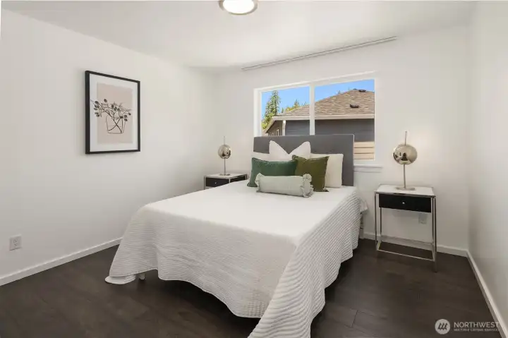 Comfortable secondary bedroom with modern finishes, wide-plank flooring, and a bright window outlook.