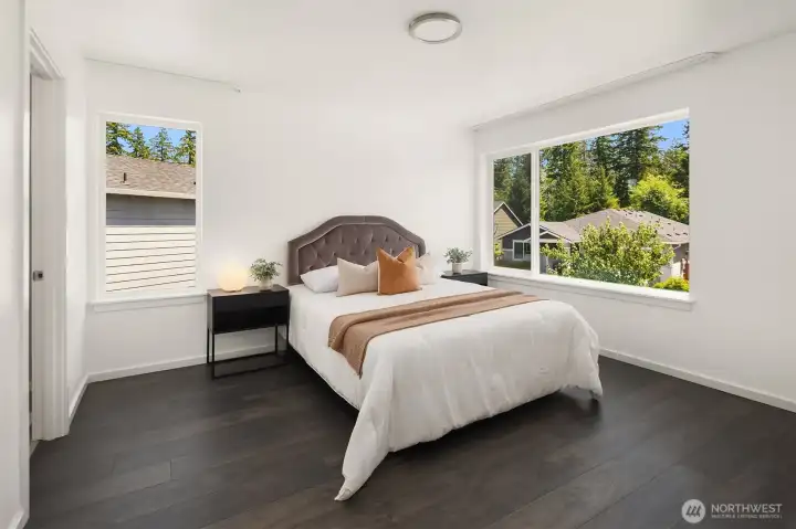 Bright bedroom with modern finishes, dark wide-plank flooring, and peaceful outlooks toward the surrounding mature landscape.
