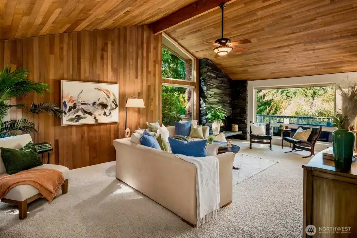 The living room showcases soaring cedar ceilings, dramatic stone fireplace, and walls of windows that blur the line between indoors and nature.