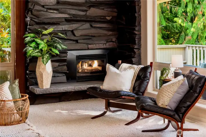 A striking stone hearth anchors the room, offering warmth and sophistication against the wooded backdrop.