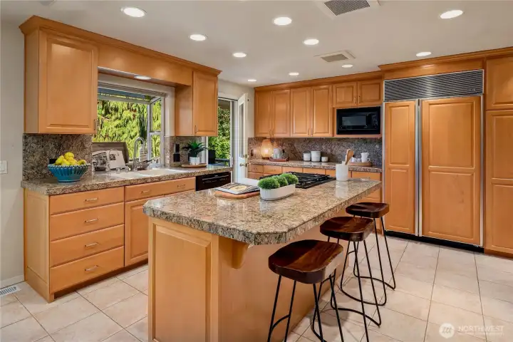 Expansive kitchen with abundant storage, gas cooktop island, and views to lush greenery beyond.