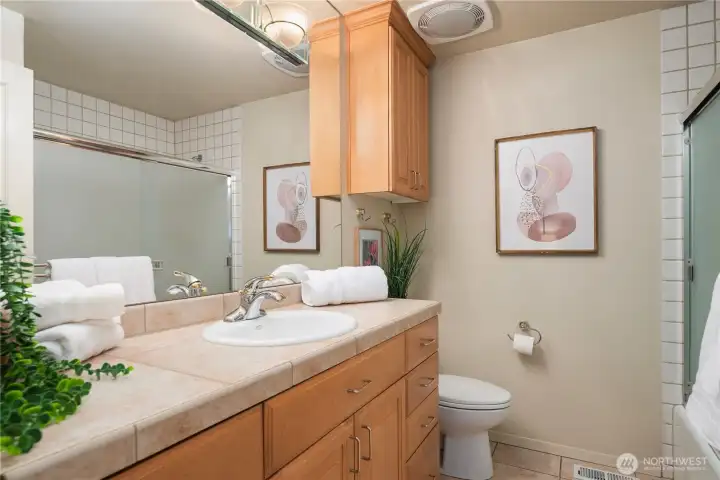 Crisp and bright full bathroom with classic tile work, ample storage, and warm wood cabinetry.