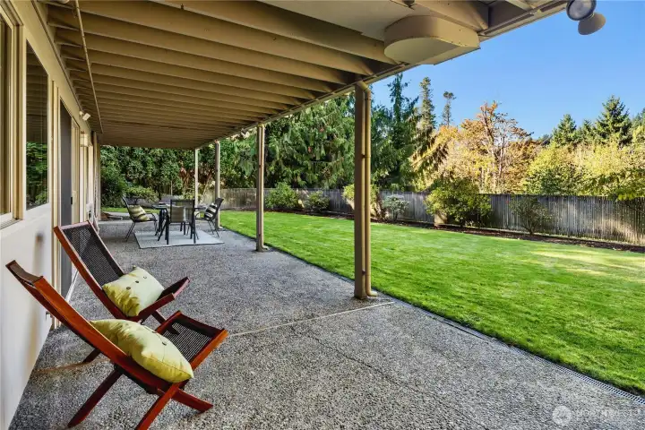 Covered lower patio opens to a sprawling, manicured lawn surrounded by evergreens.
