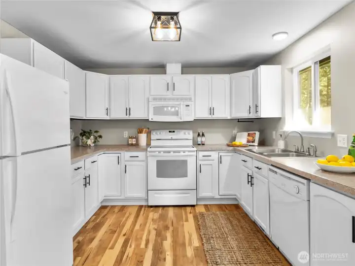 Crisp white kitchen with ample cabinet space, modern lighting, and warm wood floors throughout.