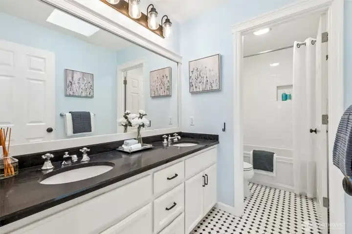 Fresh and inviting upper level bath featuring a spacious double vanity, updated fixtures and lighting, and a classic tub/shower with tile surround and built-in niche.