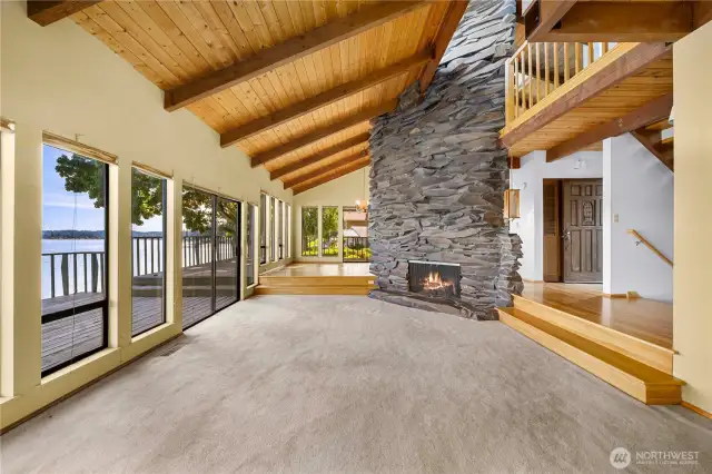 From the far end of the living room - showing the dining room to the left of the fireplace, entry to the right of the fireplace, and the stairs to the other levels on the closer right.