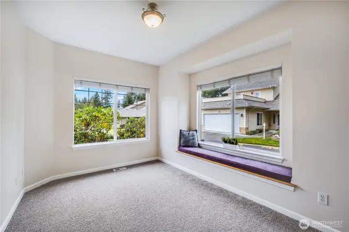 This office or bonus room located near the home’s entrance features large windows, plenty of natural light, and views of the mature landscaping surrounding the front of the home.