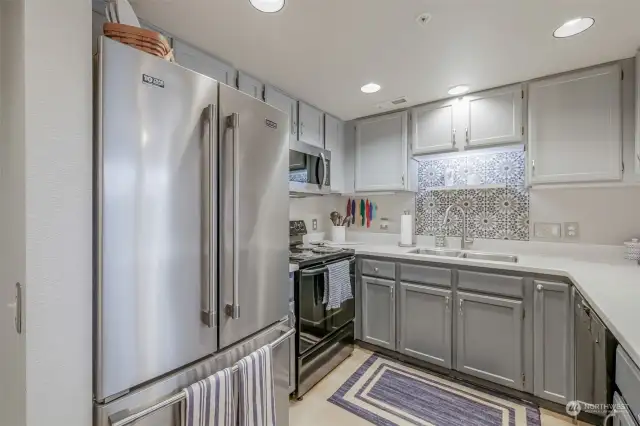 This beautifully remodeled kitchen is designed for both functionality and style. Featuring sleek stainless steel appliances, custom painted cabinetry, and an eye-catching patterned tile backsplash, this space is perfect for preparing meals with ease. Under-cabinet lighting enhances the ambiance, while recessed ceiling lights ensure a bright and inviting atmosphere.