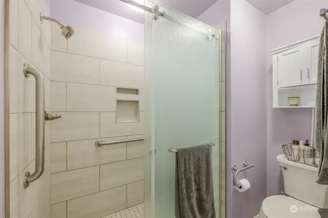 This beautifully tiled walk-in shower offers both style and accessibility, featuring a sleek glass door and safety grab bars. The combination of contemporary fixtures and thoughtful design ensures comfort and convenience.