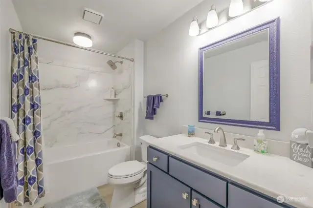 A beautifully updated bathroom featuring a modern vanity with a quartz countertop, a framed mirror, and elegant lighting. The shower and tub are complemented by stylish tilework for a spa-like experience.