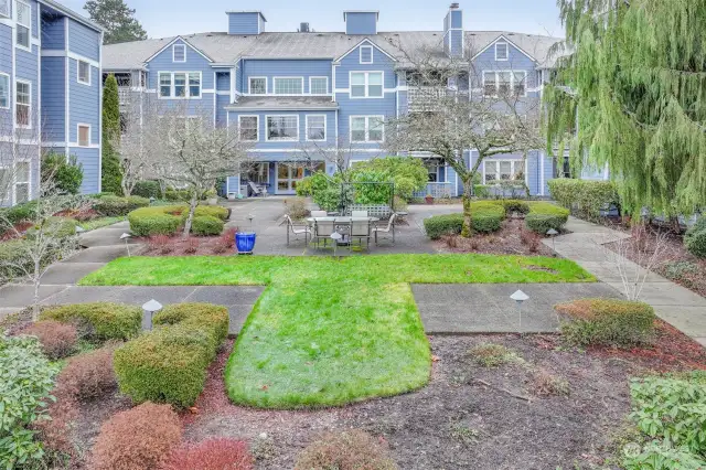 A beautifully landscaped courtyard with mature trees, manicured shrubs, and a walking path, providing a serene outdoor space for relaxation.