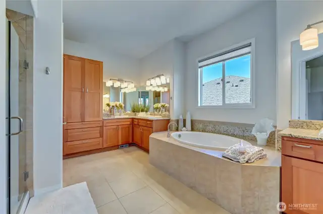 Primary en-suite with a tiled walk-in shower, separate vanities, linen storage, soaking tub, separate water closet and 1 of the 2 walk-in closets.