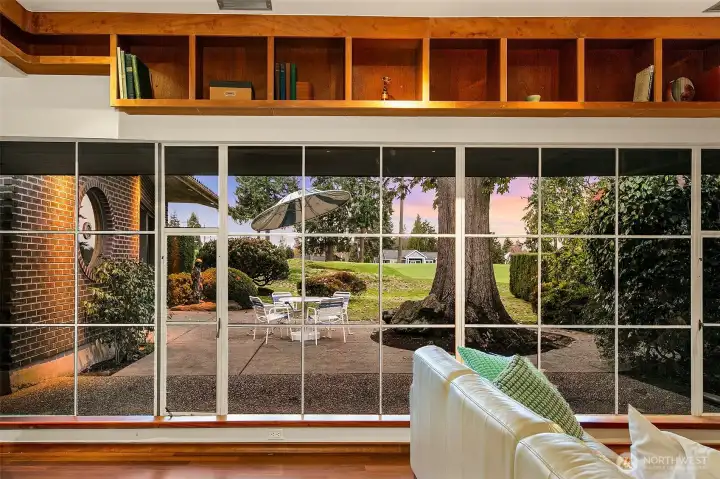 From inside the Great Room, the full-length steel window wall frames the Lanai and the heritage oak as a living mural. Floor-to-ceiling glazing brings in steady natural light and strengthens the home’s calm connection to its landscaped outdoor rooms.