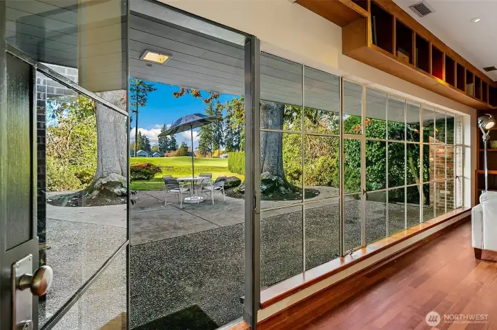 A continuous span of floor-to-ceiling commercial steel windows runs the length of the Great Room, opening directly to the Lanai and the landscaped grounds. The glazing draws in steady natural light and frames the heritage oak as a central element of the home’s indoor–outdoor rhythm.