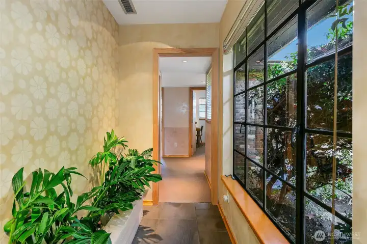 Along the bedroom-wing hall, a built-in planter with integrated irrigation and drainage brings living greenery into the passage. Custom Venetian-plaster walls and a floor-to-ceiling steel window create a soft mix of craft, light and texture as the hall leads toward the private rooms.