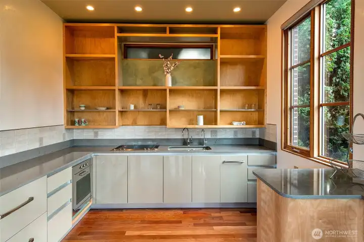 The bungalow’s full kitchen is outfitted with tailored millwork, open cedar shelving, and stainless counters that wrap the room. A two-burner Wolf cooktop, Bosch oven, and integrated refrigeration support independent living, while the large window brings in garden light that plays across the joinery. This space reflects the same level of craft found throughout the bungalow, designed for guest use, extended stays, or creative work.