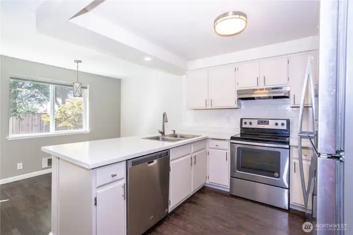 Wide kitchen view with breakfast bar, stainless appliances and wood flooring.