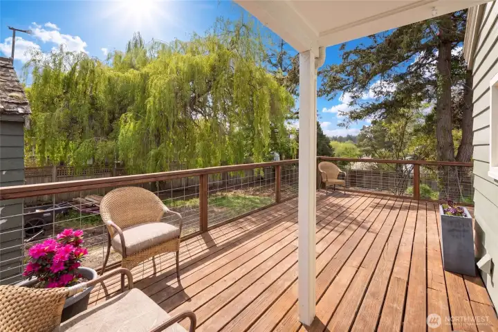 The expansive elevated deck offers sweeping westward views over lush treetops, framed by a graceful weeping willow, positioned to enjoy San Juan Island's legendary sunsets. The wood decking creates an inviting outdoor living space ideal for year-round enjoyment.