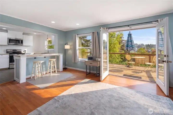 Sun-drenched open-concept living and dining area flows seamlessly through French doors onto the spacious deck, capturing westerly views over the treetops with beautiful natural light pouring in. The updated kitchen peninsula with butcher block counters and bar seating anchors the social heart of this thoughtfully remodeled 1940 charmer.