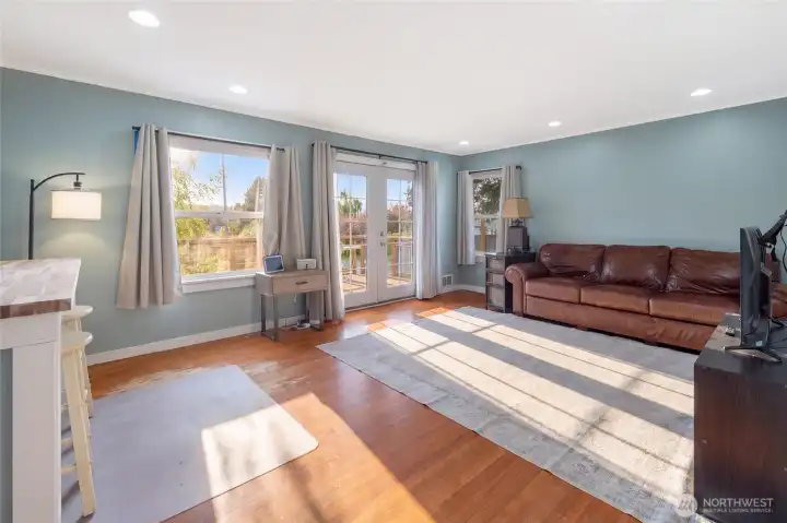The airy, light-filled living room boasts soft blue-gray walls, recessed lighting, and three exposures of natural light with French doors opening to the expansive outdoor deck — perfect for relaxed island living.