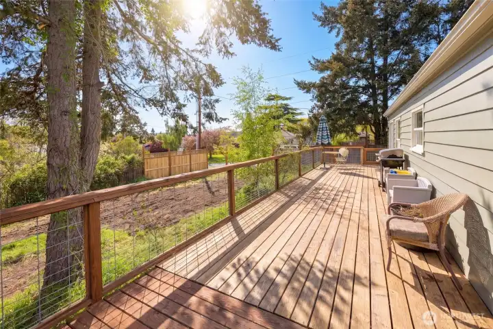 The generous deck extends the full length of the home, offering elevated views of the spacious fenced yard and mature evergreens beyond — an entertainer's dream in a quiet residential setting. Whether hosting summer barbecues or enjoying a peaceful morning coffee, this outdoor space embodies the best of island living.