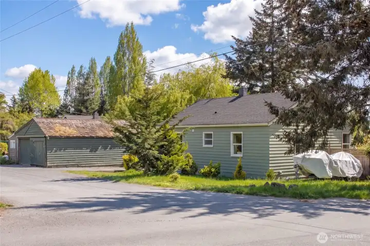 The expansive corner lot offers abundant outdoor space with mature landscaping including towering conifers and lush greenery, while the detached garage and generous driveway provide versatile utility. Multi-family zoning for up to four units (buyer to verify) positions this property as a rare opportunity in the heart of Friday Harbor.