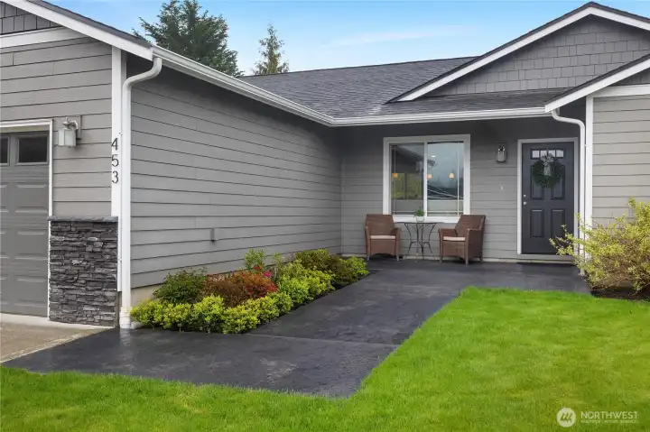 Welcome guests from the stamped and stained front patio, framed by tidy landscaping and a covered entry.