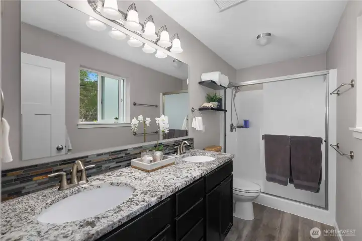 Refresh in the primary bath with dual sinks, granite-style counters, tile backsplash, and a walk-in shower.