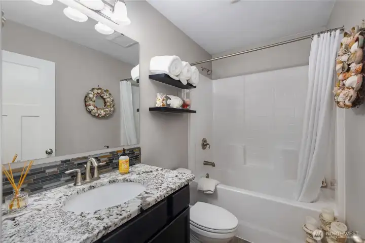 Full guest bath with granite-style counter, tile backsplash, and clean tub/shower surround.