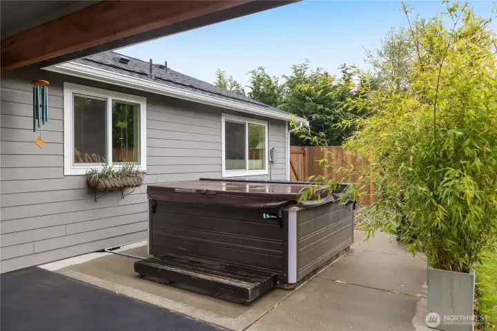 Negotiable salt-water hot tub privately tucked near the covered patio and backyard greenery.