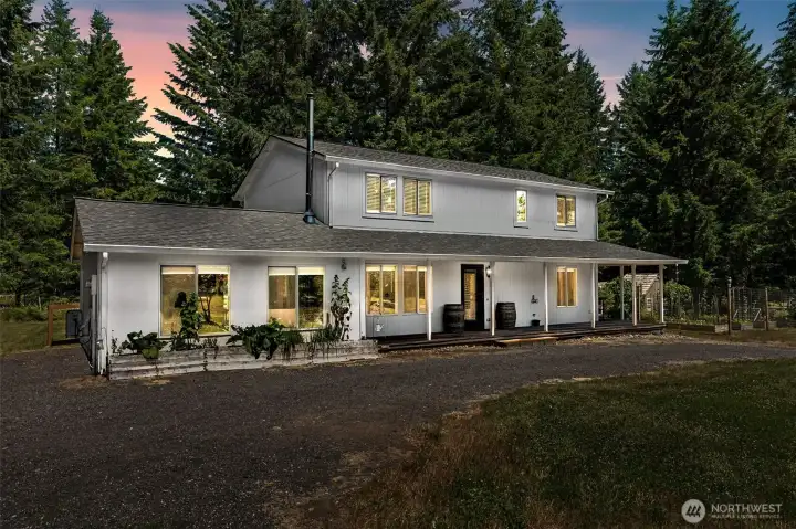 If homes could give hugs, this one absolutely would. This twilight view captures the warmth and charm that make this property feel so special. Soft light spills from the windows onto the expansive wraparound covered porch, creating the kind of welcoming atmosphere that practically begs for rocking chairs, morning coffee, and long conversations at sunset. One of the most unique features of the home is the former attached garage space, which has been thoughtfully converted into additional living area. The large picture windows you see here are newer Andersen double-pane windows that flood the bonus space with natural light while adding tremendous curb appeal. A brand-new roof provides added peace of mind, and the circular driveway allows guests to arrive right at the front porch with ease.