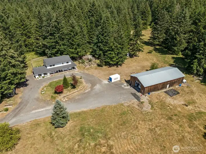 This is where the property starts telling its story. The aerial perspective highlights the thoughtful layout of the five-acre parcel, with the home and impressive 2,450-square-foot shop positioned to complement one another beautifully. The circular driveway functions almost like a private roundabout, making arrivals, departures, guests, trailers, and everyday life remarkably easy. One of the biggest advantages here is that the shop isn't attached to the home's daily living spaces. Whether you're woodworking, wrenching, creating, storing, or entertaining, activities can happen over there while life remains peaceful over here. You'll also notice the gardens surrounding the home and the sea of evergreens wrapping the property in privacy. Living near Capitol Forest has its perks, and one of the biggest is feeling immersed in nature while still enjoying the convenience of a well-planned property like this.