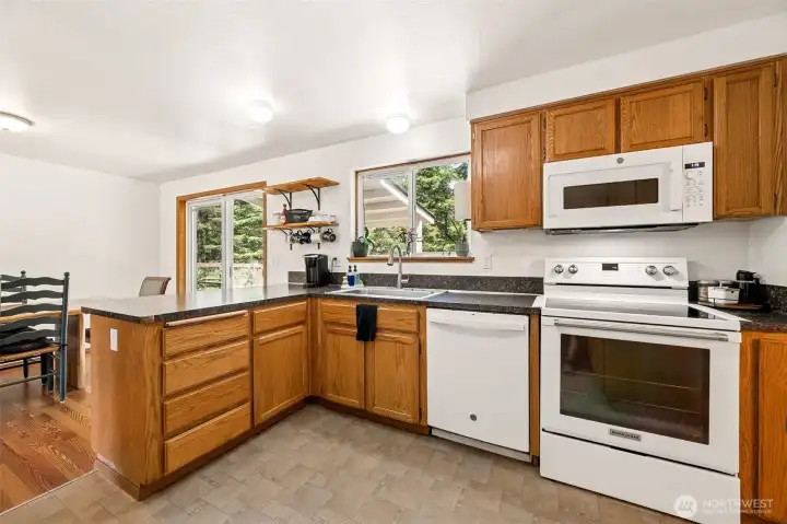 Between the large window over the sink and the sliding glass door nearby, sunshine pours into the space and helps create a bright, cheerful atmosphere for everything from morning coffee to holiday baking sessions. This view also provides a closer look at the KitchenAid electric range and GE convection microwave, a combination that offers flexibility for everyday cooking and entertaining alike. Tucked into the cabinetry is a clever pull-out cutting board, one of those old-school practical features that homeowners often find themselves using every day.