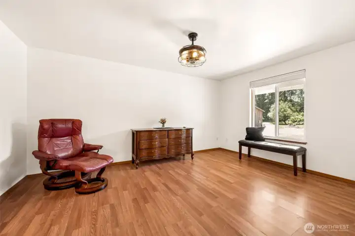 One of the biggest advantages of this floorplan is that the primary suite is located on the main level, allowing the home to adapt beautifully through every stage of life. This spacious retreat offers plenty of room for a king-size bed, multiple dressers, a cozy seating area, or even a reading nook by the window. Natural light pours through the large front-facing window, while the blinds allow you to customize privacy and light levels whenever you'd like. The warm wood-look flooring continues into the room, pairing beautifully with the crisp white walls to create a bright, welcoming atmosphere. Overhead, another one of the home's clever retractable fan-light fixtures provides both stylish illumination and efficient air circulation when needed.