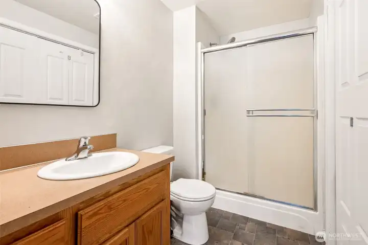 The main-level primary suite enjoys the convenience of its own private three-quarter bathroom, thoughtfully designed with easy maintenance in mind. A long vanity provides plenty of countertop space for daily routines, while the warm oak cabinetry below offers generous storage for toiletries, linens, and personal items. The Formica countertop is durable and easy to care for, making it a practical choice for everyday living. You'll also find waterproof vinyl flooring underfoot and a glass-enclosed shower featuring privacy glass for added comfort.