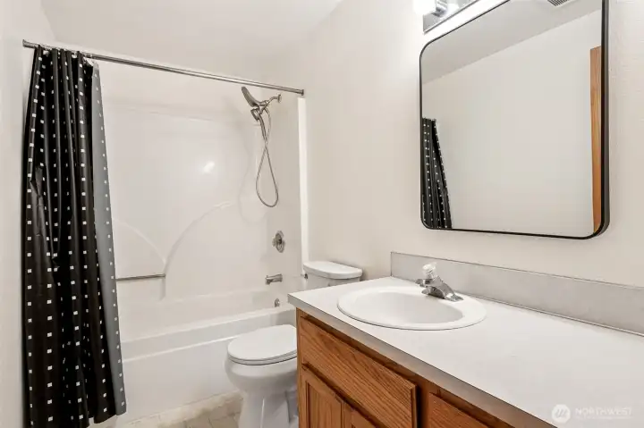 Conveniently located on the second floor, this full bathroom serves the upstairs bedrooms with a layout that's as practical as it is comfortable. The extra-long vanity provides plenty of elbow room, while the oak shaker cabinetry offers excellent storage beneath the durable Formica countertop. Waterproof vinyl flooring makes cleanup simple and stands up beautifully to everyday life. The fiberglass tub and shower surround is complemented by a dual showerhead fixture, bringing a spa-inspired touch to a space that's built for functionality.