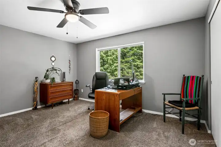 Wake up to the beauty of the Pacific Northwest every morning from this inviting upstairs bedroom. Approximately 14' x 11', the room offers plenty of space for comfortable furniture arrangements while maintaining a cozy, relaxing feel. Soft neutral finishes, including plush mushroom-toned carpeting, gray walls, and bright white trim, create a timeless palette that's easy to make your own. A ceiling fan adds comfort throughout the seasons, and the large window brings in natural light while overlooking the peaceful forested surroundings. It's another reminder that while you're only minutes from shopping and amenities, home still feels like your own private woodland retreat.