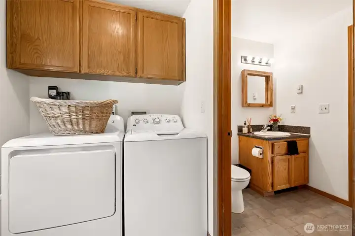 Positioned next to the backyard entrance, this laundry room naturally functions as a mudroom, making it easy to transition between outdoor adventures and indoor comfort. Whether you've been tending the garden, working in the shop, exploring the acreage, or simply enjoying the outdoors, this is the ideal place to kick off your boots and clean up. The washer and dryer stay with the property, while the warm oak cabinetry offers plenty of storage overhead. We also love that the half bath is enclosed in its own separate room rather than sharing the laundry space, creating added privacy and convenience for family members and guests alike.