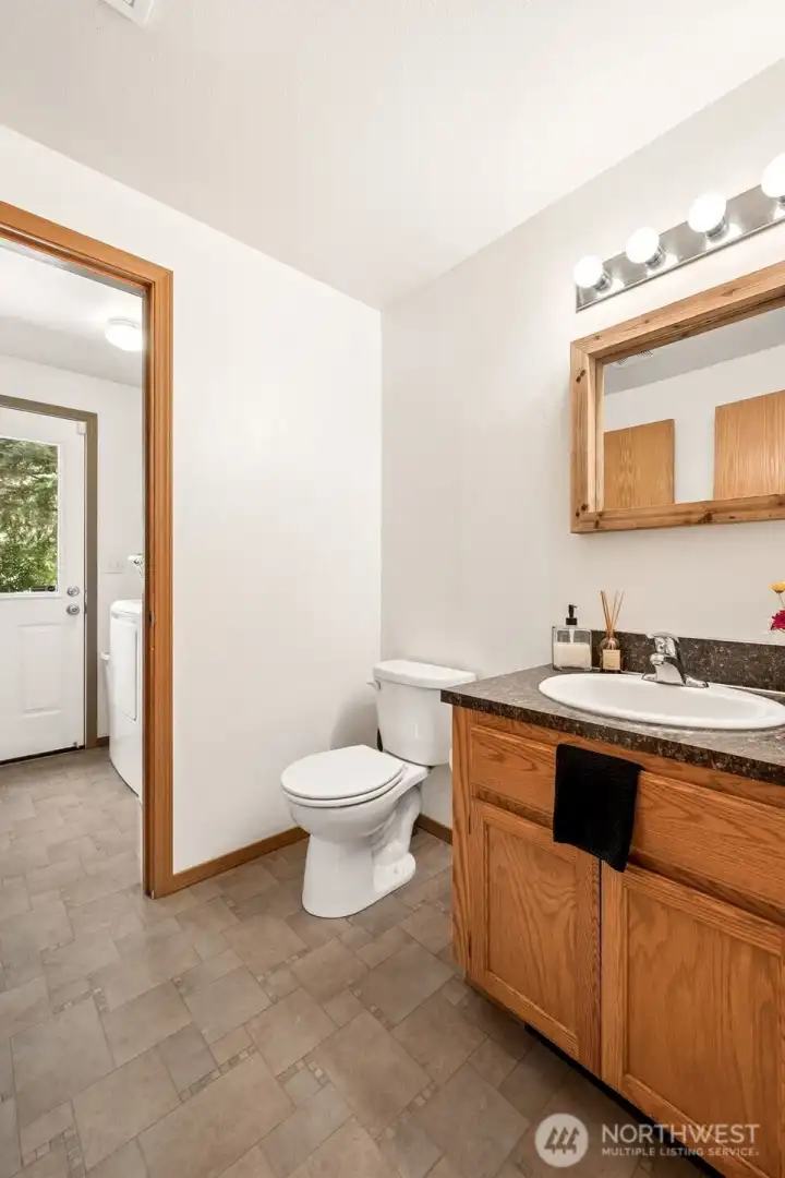 Whoever designed this part of the home understood exactly how country properties work. The backyard door leads directly into the mudroom/laundry area, with this convenient half bath right alongside it. It's the perfect arrangement for gardeners, hobbyists, shop enthusiasts, pet owners, or anyone who occasionally comes inside wearing a little evidence of their outdoor adventures. The spacious vanity provides useful storage, while the warm oak cabinetry and coordinating wood-framed mirror help the room feel inviting rather than purely utilitarian. Easy-care waterproof flooring runs throughout the area, making cleanup simple and stress-free. Functional? Absolutely. Clever? Definitely.
