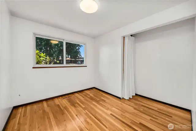 Light-filled bedroom featuring refinished hardwood floors and a wide quadruple-pane window that enhances both natural light and noise reduction. A cozy closet offers flexible storage, while neutral walls make this space easy to personalize for use as a bedroom, office, or guest room.